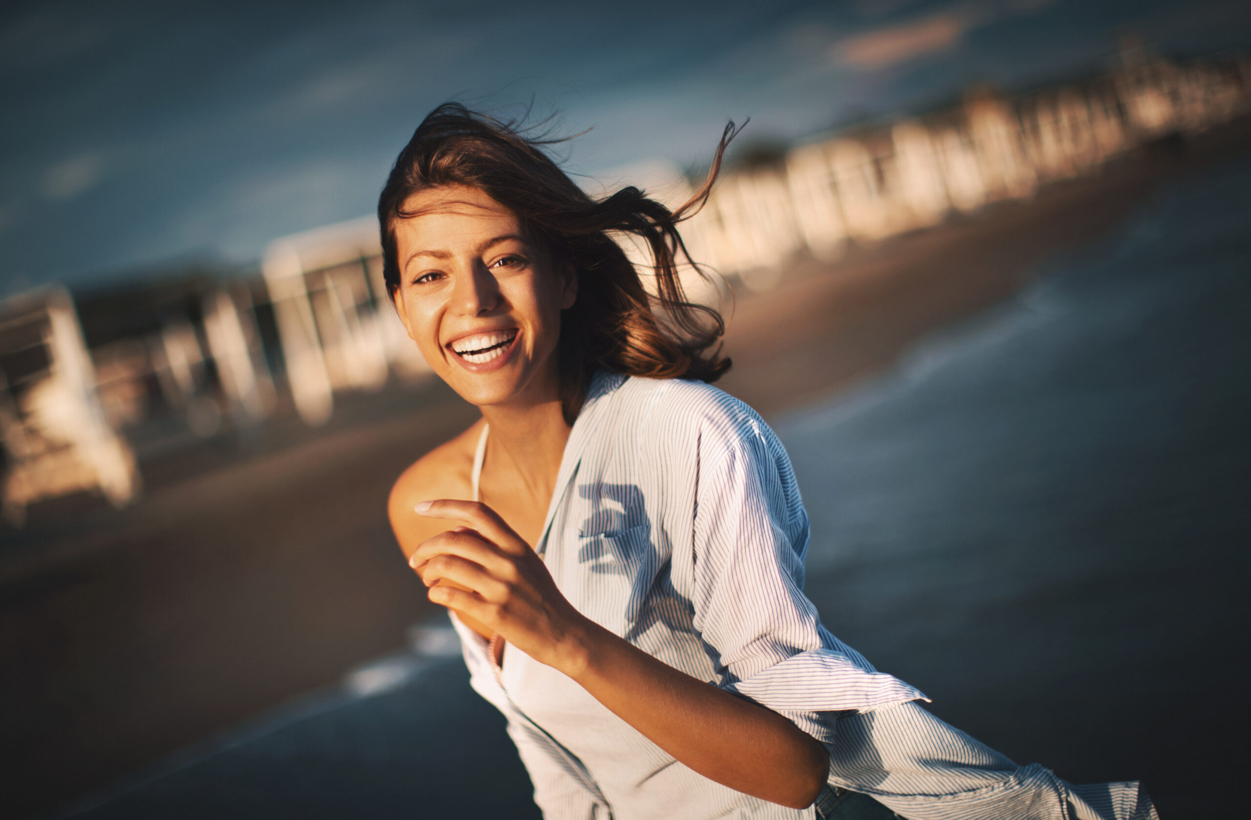 Closeup front view of an attractive mid 20's brunette walking on the beach at sunset and flirting with the camera. She's wearing men's shirt.